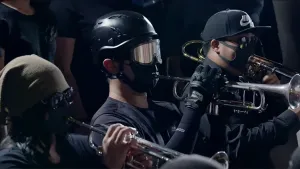 Foto van trompetblazers in protestmars die donker gekleed zijn, één ervan heeft een helm op.