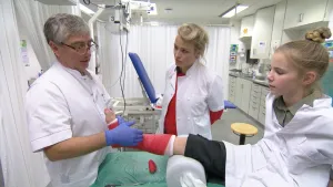 Foto van meisje op bed in Röntgenkamer (ziekenhuiskamer) met arts en verpleegster erbij.