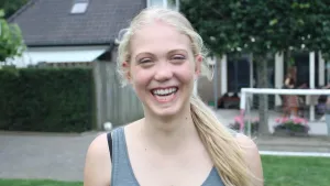 Foto van het gezicht van een lachend meisje met schisis buiten op straat.