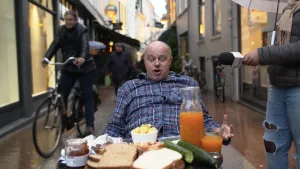 Foto van een man zit in een straat met fietsers aan tafel met daarop een uitgebreid ontbijt.