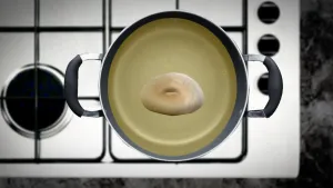 Foto van een pan met bakvet/olie op een fornuis van bovenaf gezien, in die pan ligt een donut.