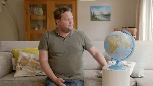 Foto van presentator die op een bank zit bij een wereldbol (globe).