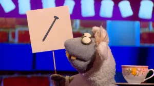 Foto van Boterhamshow waarbij Nico de Neushoorn aan tafel gedicht voordraagt en houdt tekening van een spijker vast.