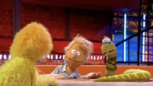 Foto van Boterhamshow met Steef Stronk (man, pop) aan tafel zit bij Opperdepop, op de tafel ligt een slang (van stof).