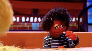 Foto van uitzending Boterhamshow met Lisa (pop) die aan tafel zit bij Opperdepop en bezig is met luizen te verzamelen.