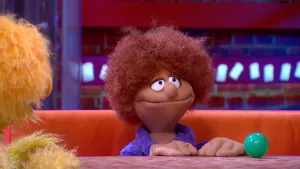 Foto van de Boterhamshow waarbij Barbara Bank (een pop) aan tafel zit met een grote groene knikker, je ziet nog stukje van Opperdepop.