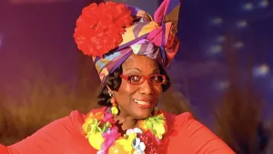 Foto van uitzending van Sesamstraat met vrouw, vrolijk gekleed, die zingt.