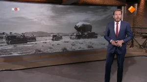 Foto van presentator in pak voor een scherm met foto's van voertuigen uit de Tweede Wereldoorlog.