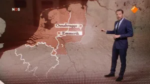 Foto van beeld uit het NOS-Journaal waarop de nieuwslezer staat bij een oude kaart van Nederland en omringende landen in 1945.