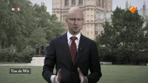 Foto van beeld uit het NOS-Journaal met nieuwslezer Tim de Wit met op de achtergrond deel van het Britse Parlement.