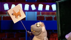 Foto van scène in Boterhamshow met pop, Neushoorn, die gedicht voordraagt en plaatje van een hond vasthoudt.