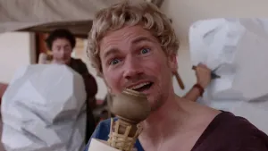 Foto van portret van man verkleed als Romein met twee Griekse beelden erbij.