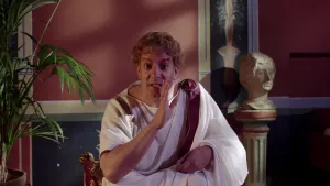 Foto van man verkleed als Keizer Claudius, binnen in Romeinse woonkamer.