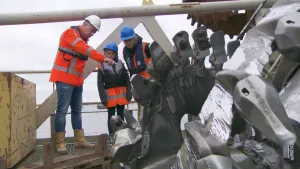 Foto van drie mensen met een bouwhelm op een stellage.