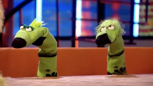 Een foto van twee groene sokken met zwarte punten aan het uiteinde en zwarte vormen van sneeuwvlokjes erop achter een bruine tafel. De sokken hebben een gezicht met ronde ogen bovenop. De ene heeft een groen plukje haar en de ander krullend groen haar.