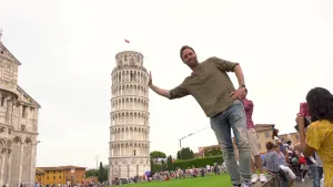 Een foto van Bart die op een muurtje staat naast een groen grasveld. Op de achtergrond staat de toren van Pisa, een witte, ronde, scheefstaande toren van zeven verdiepingen. Op de foto lijkt het net of Bart zijn rechterhand tegen de scheve toren aanlegt.