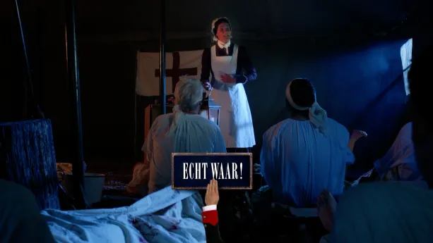 Een foto van een vrouw verkleed als Florence Nightingale in een witte schort en met wit kapje op haar hoofd in een grote, blauwe tent verlicht door een soort maanlicht. Twee mannen zitten naar haar te kijken. Vóór de foto staat "Echt waar!" op een bordje.