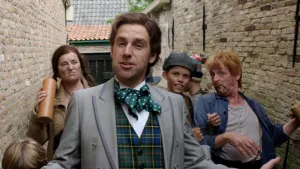 Een foto van een man ineen grijs pak, een geruite blouse en met een groene strik met witte stippen om zijn nek. Erachter staan een man en een vrouw die een lichtbruine kruik met drank erin vasthebben en een jongen die lachend naar de camera kijkt.