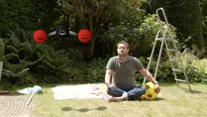 Een foto van Diederik in kleermakerszit op een handdoek op een grasveld. Eén van zijn armen ligt op een geel met zwarte bal.  Ook staat er een tekening boven van drie lachende gezichtjes die met een lijntje aan elkaar zitten, twee rood en één zwart.