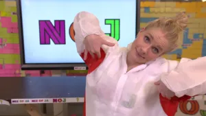 Een foto van presentator Janouk die in de studio staat en zichzelf in haar oksels aan het kietelen is.