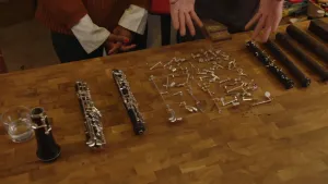 Een foto van een tafel waarop onderdelen van het blaasinstrument hobo liggen. Er liggen drie delen van de zwarte houten buis van de hobo met zilverkleurige stukjes erop, zilverkleurige druktoetsen of klepjes en vier buizen voor de binnenkant van de hobo.