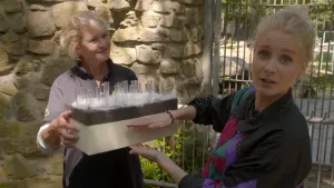 Een foto van Janouk die haar handen voor een rechthoekig blok houdt, dat een vrouw ernaast vastheeft. Op het blok zit onderaan een witte zachte stof, zoals watjes, en steken ronde, glazen buisjes omhoog. Het is een voorbeeld van de huid van een ijsbeer.