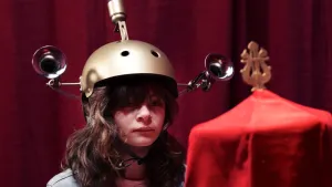 Een foto van Fief, die een helm opheeft met aan beide kanten een soort toeter en bovenop ook een omhoogstaand, ovaal ding. Fief kijkt naar een ding, een soort kleine tent, met een rode doek erover. In de aflevering ziet ze een concert achter het doek.