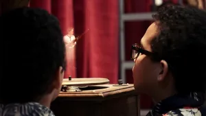 Een foto van Rayan en Mehdi die kijken naar een houten platenspeler met een draaiende cirkel of schijf, zonder plaat met muziek erop. Erboven is een driedimensionaal voorbeeld van een man te zien die op een fagot, een langwerpig blaasinstrument, speelt.