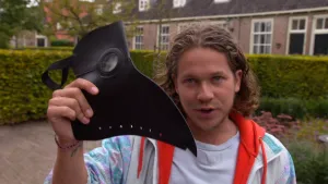 Een foto van Pascal die een zwart masker voor de camera houdt. Het masker lijkt op de kop met snavel van een vogel zoals een kraai. Een dokter in de veertiende eeuw, die ook wel de snaveldokter genoemd werd, droeg dit masker als bescherming tegen de pest.