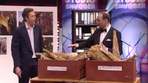 Een foto van Han en een presentator met ervoor een tafel met twee bruine bakken. Er zitten bruine, pegelvormige stukken in uit een grot, stalactieten in de linkerbak die van het plafond groeien en stalagmieten in de rechterbak die op de grond groeien. 