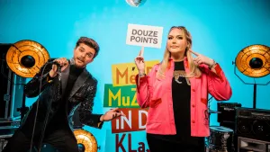 Een foto van Buddy in een zwart, glanzend pak die een microfoon vastheeft en zingt. Nikkie de Jager staat ernaast in een rood vest en zwart t-shirt met een panter. Ze wijst naar het bordje in haar hand met daarop "douze points", Frans voor twaalf punten.