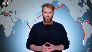 Een foto met daarop een presentator en daarachter een deel van de kaart van de wereld. Er zijn rode lijnen op de kaart getekend waar aardbevingsgevaar is: op het land is dat onderaan in Azië, langs het Amerikaanse continent en rechts onder Europa.