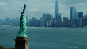 Een foto van het vrijheidsbeeld in de Verenigde staten aan het water. De zijkant met de omhoogstekende arm met fakkel in de hand is te zien. De kleur van het beeld hangt tussen groen en blauw in. Het beeld is van een vrouw, de Romeinse godin Libertas. 