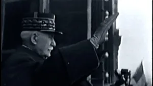 Een zwart-wit foto van Charles de Gaulle in Frankrijk in 1944. Hij draagt donkergekleurde kleding en een donkergekleurde pet. Hij zwaait met een gehandschoende hand naar het niet-zichtbare publiek. Rechtsonder is een stuk van een vlag te zien. 