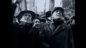 Een zwart-wit foto genomen in Praag in 1948 van mensen die blij juichen. Twee mannen en één vrouw zijn met gezicht in beeld. Ze dragen een jas, één man een hoed en de andere twee een pet. Erachter steken vlaggen omhoog, waarvan de opdruk niet te zien is.