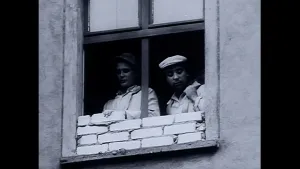 Een zwart-wit foto van twee mensen achter een geopend raam van een gebouw of huis. Eén van de mensen is bezig om het raam dicht te metselen met cement en bakstenen. De persoon links zet de tweede steen op de vierde laag van stenen.