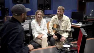 Een foto van Edson, die samen met Suzan en Freek in een geluidsstudio zit. Rechtsvoor staat op een tafel een opengeklapte koffer met een platenspeler erin, met een gouden plaat van Suzan en Freek erop. Het is een zwartgekleurde LP met een gouden glans. 