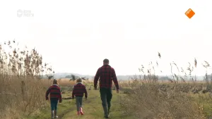 Een foto van boswachter Tim en twee jonge kinderen. Ze lopen in de natuur, van de camera weg. In de verte zie je ganzen op de grond zitten.
