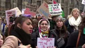 Een foto van een groep vrouwen die borden omhooghouden over de gelijkheid van man en vrouw. Ze demonstreren tegen seksueel grensoverschrijdend gedrag van mannen, die dingen doen die ze niet willen. Op de achtergrond zijn ramen te zien van een gebouw. 