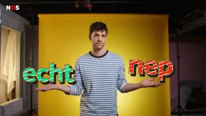 Een foto van een presentator die met gespreide armen voor een geel doek staat. Links staat boven zijn arm in groene letters "echt", rechts staat boven zijn arm in rode letters "nep".