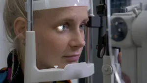 Een foto van presentator Janouk die een oogmeting laat doen met een speciaal apparaat bij een brillenspecialist.