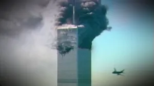 Een foto van de bovenkant van één van de torens van het World Trade Center tijdens de terroristische aanslag op 11 september 2001. Er komen dikke, donkere rookwolken uit, want er is een vliegtuig ingevlogen. Een tweede vliegtuig vliegt ernaartoe.