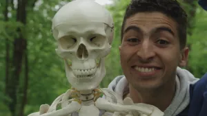 Een foto van presentator Nizar die buiten naast een skelet staat. Bijna alleen hun hoofden zijn zichtbaar in de foto.