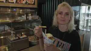 Een foto van presentator Janouk die in een snackbar wat friet met mayonaise aan het eten is.