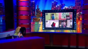 Een foto met twee poppen: Sydney May die zit, en een pop van een presentator die staat. Ze kijken met hun rug naar de camera naar een beeldscherm met daarop een beeld van vier mannelijke en twee vrouwelijke poppen op een aparte foto. Drie dragen een bril.