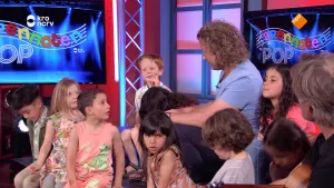 Een foto van presentator Pepijn in de Tv-studio van Apennoten. Hij zit tussen kinderen en praat met hen. 