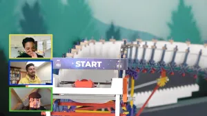 Een foto van een knikkerbaan. Je ziet het start-punt, met een knikker die klaar ligt. Links in beeld zie je drie rechthoeken met daarin de presentatoren van dit programma die meekijken.