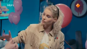 Een foto van presentator Janouk. Ze is in een studio. Op de achtergrond zie je rode en roze ballonnen.