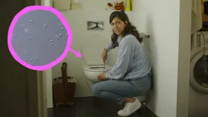 Een foto van Manon die op haar hurken zit voor een witte wc. Ze houdt een toiletborstel in de wc en kijkt met een ongemakkelijke blik naar de camera. In een roze cirkel met pijl die naar de wc wijst, staan witte bolletjes op een grijze achtergrond.