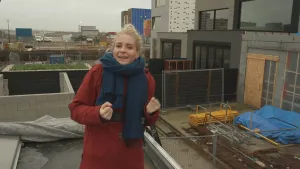 Een foto van presentator Janouk die op een dak staat tussen allemaal bouw terreinen in.